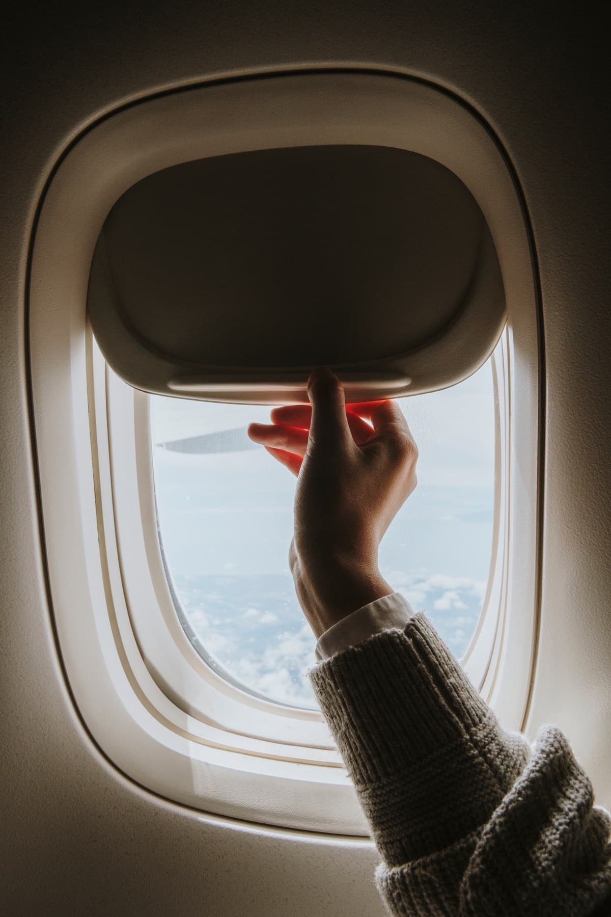 Mão abrindo a janela de um avião durante o voo